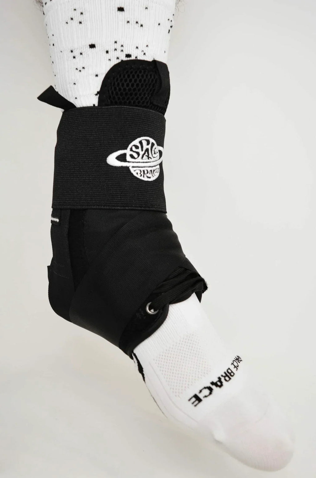 Black ankle support brace with white embroidered logo worn over white sock