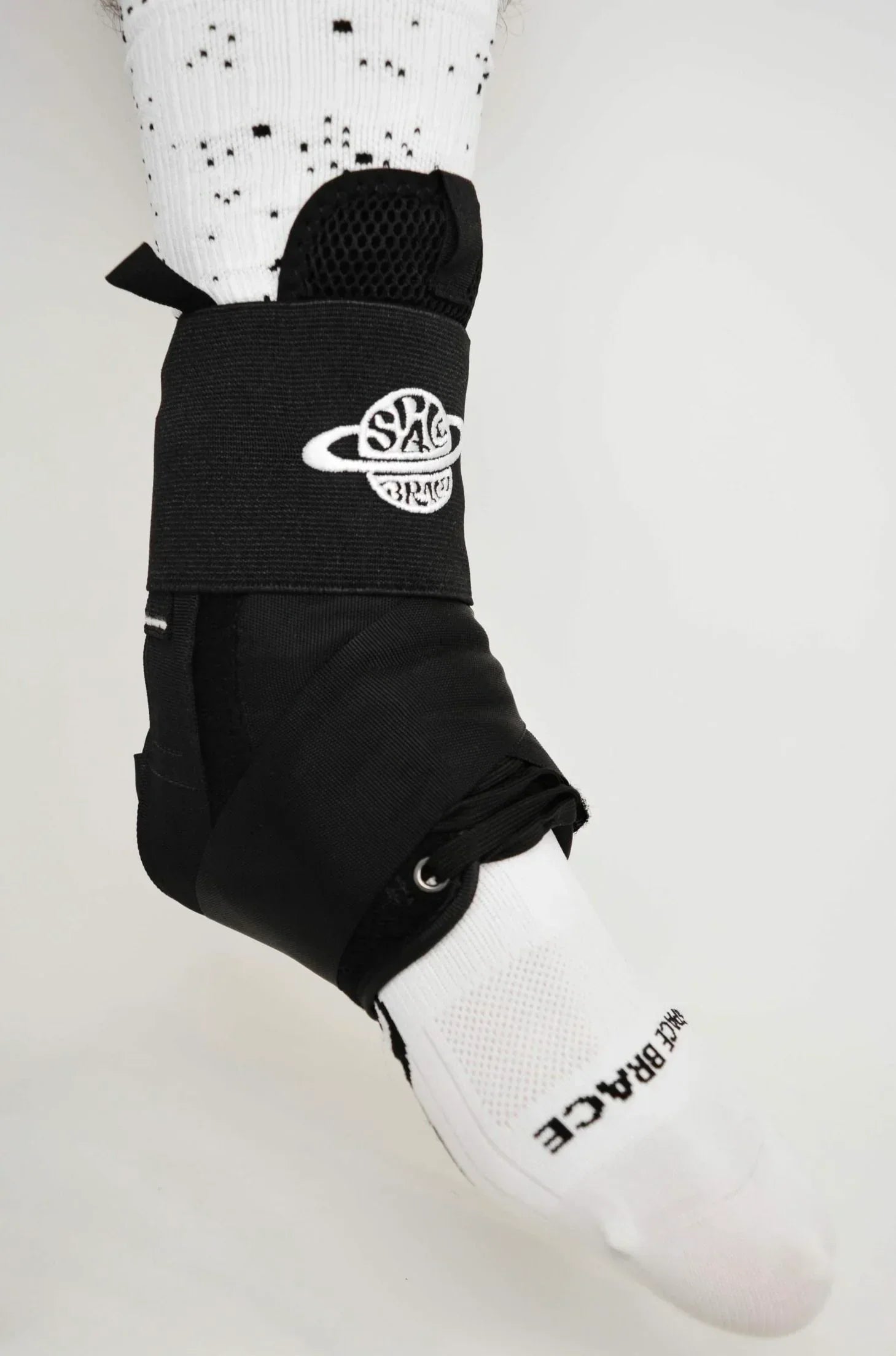 Black ankle support brace with white embroidered logo worn over white sock