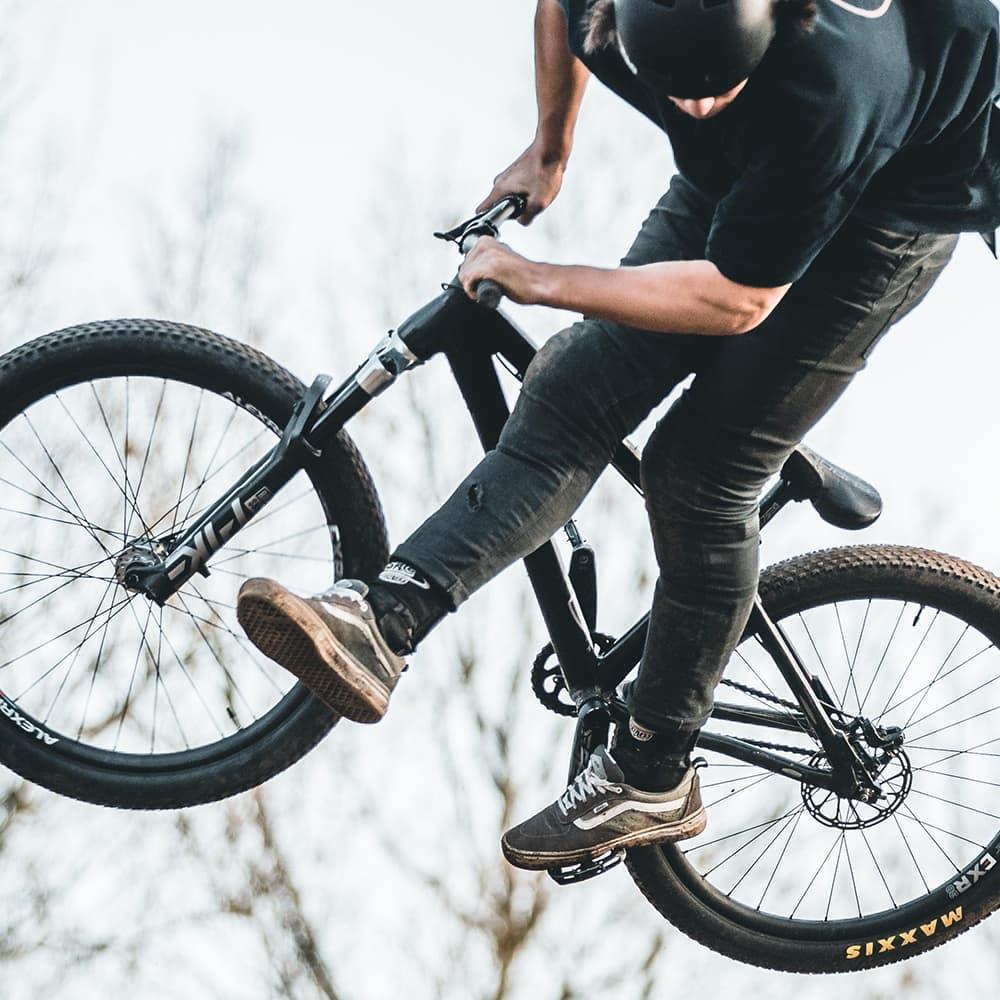 BMX rider mid-air performing trick, wearing helmet, ankle brace, and casual shoes.