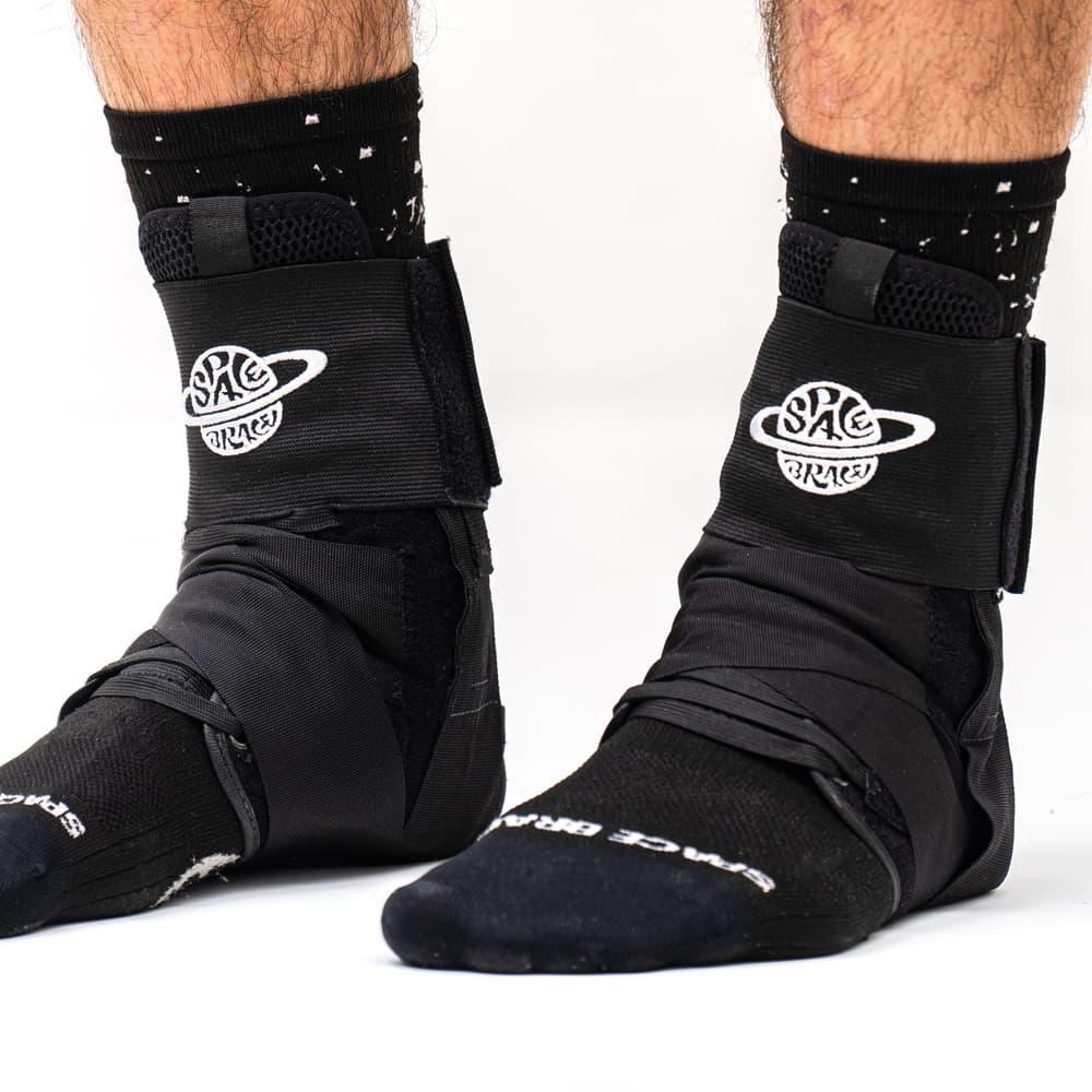 Person wearing black ankle braces over black socks, close-up on feet