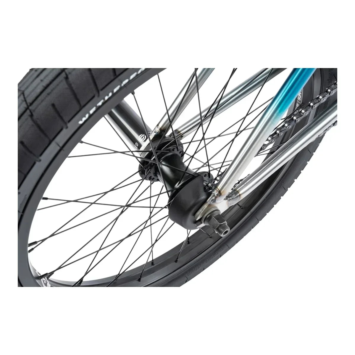 Détail roue BMX avec pneu WETHEPEOPLE, moyeu noir et chaîne, cadre métal bleu et argent