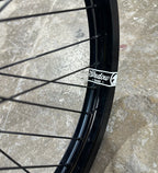 Roue BMX noire Shadow Conspiracy avec étiquette 'Shadow Russ' sur fond de béton