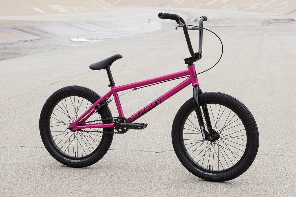 Vélo BMX rose avec pneus noirs sur un sol en béton gris