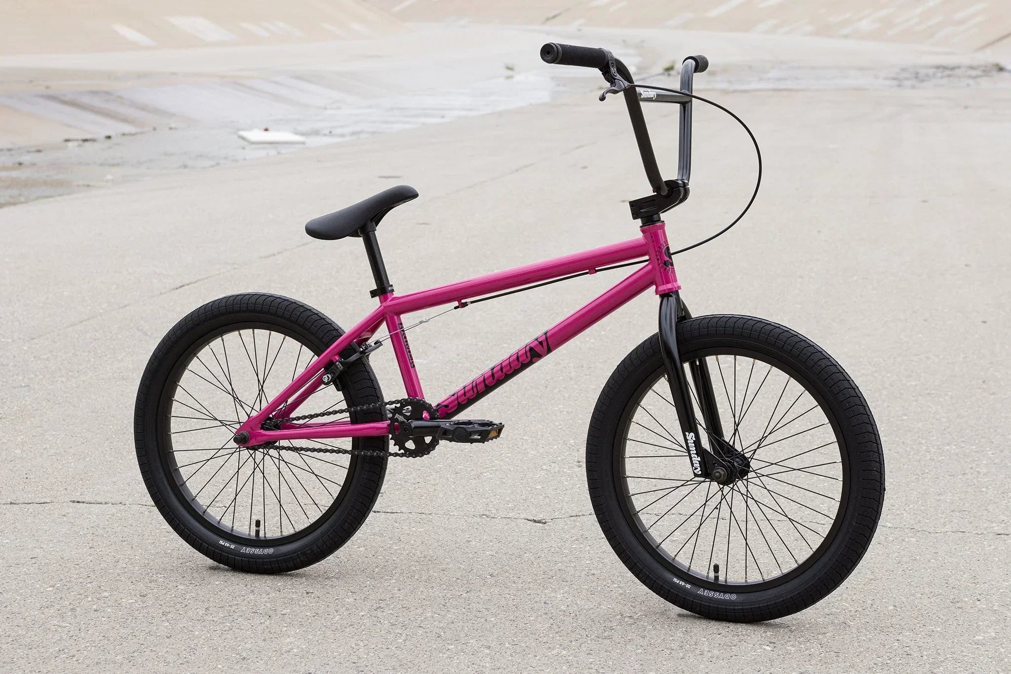 Vélo BMX rose avec pneus noirs sur un sol en béton gris