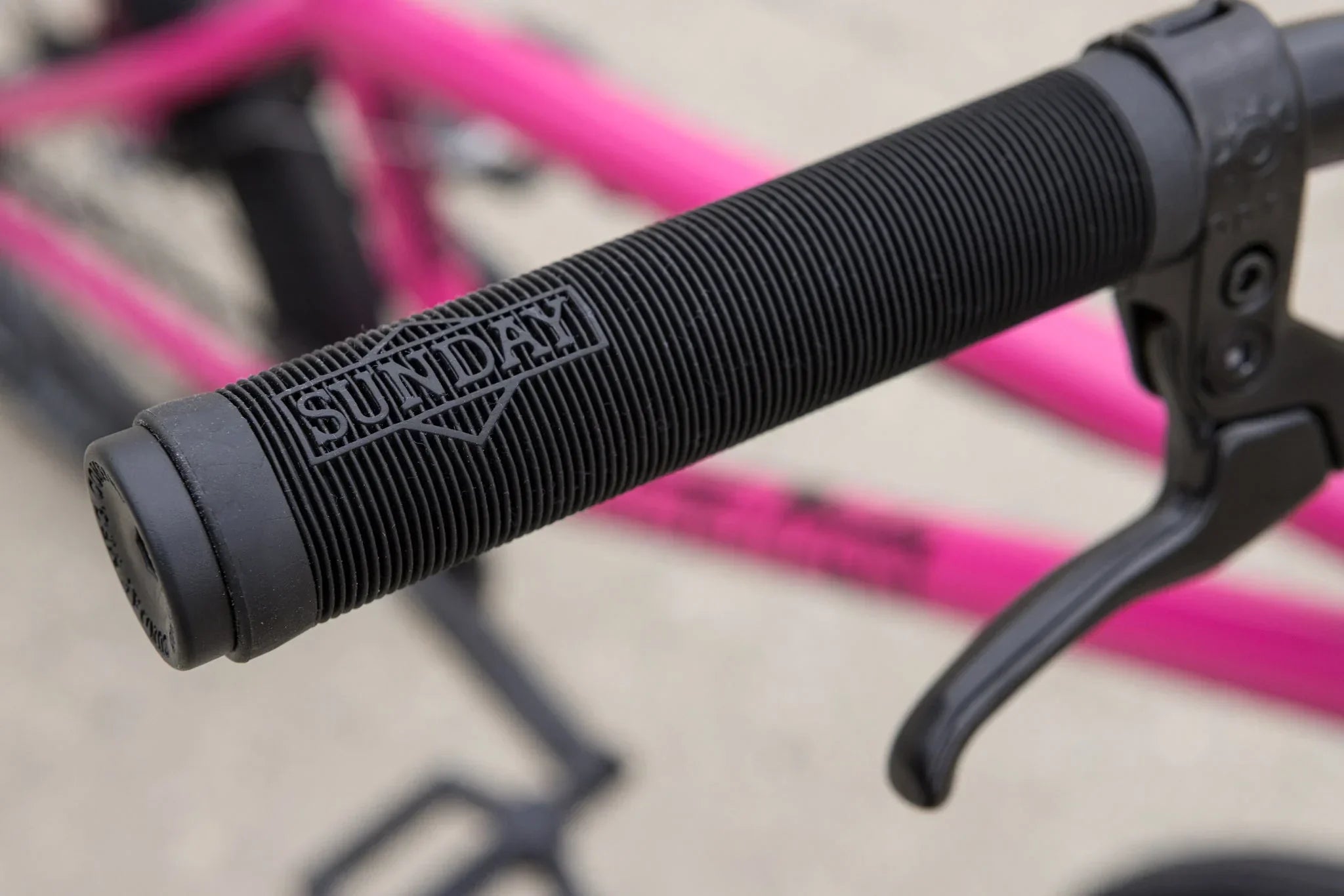 Gros plan d'une poignée de guidon BMX noire Sunday sur un cadre de vélo rose vif.