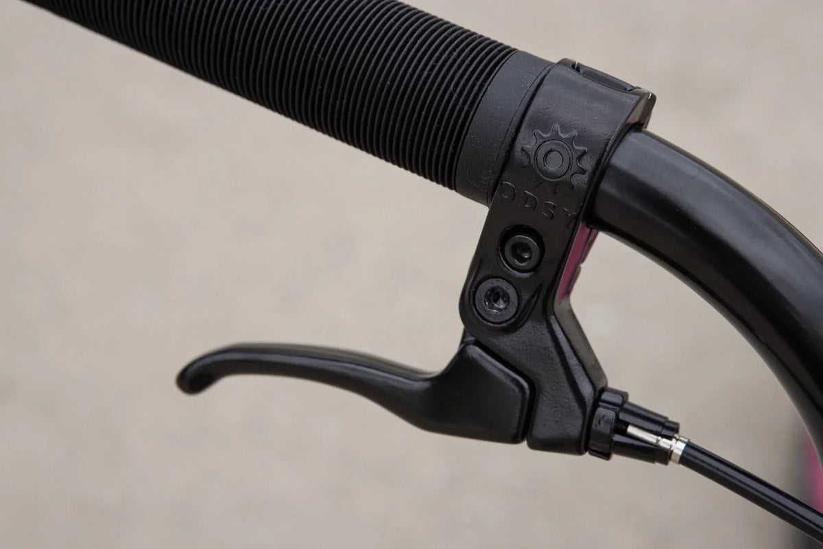 Gros plan d'un levier de frein noir Odyssey installé sur un guidon de BMX.