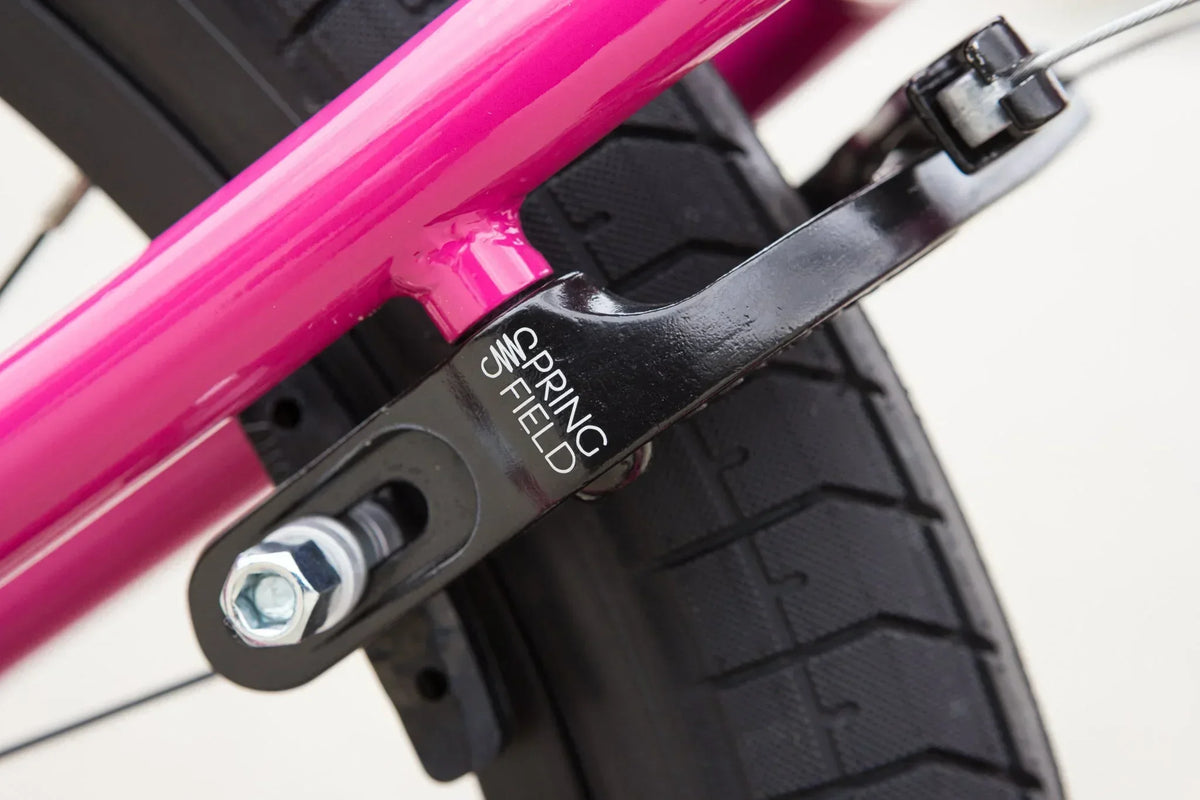 Détail du frein arrière noir Spring Field sur un cadre de vélo BMX rose vif.