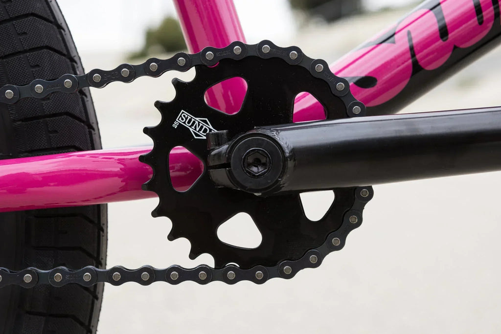 Gros plan d'un plateau de pédalier Sundae noir sur un cadre de vélo BMX rose vif