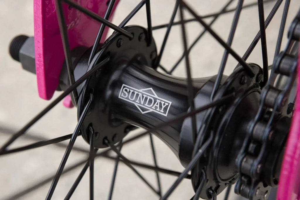 Gros plan d'un moyeu de roue BMX noir de marque Sunday avec rayons et cadre rose.