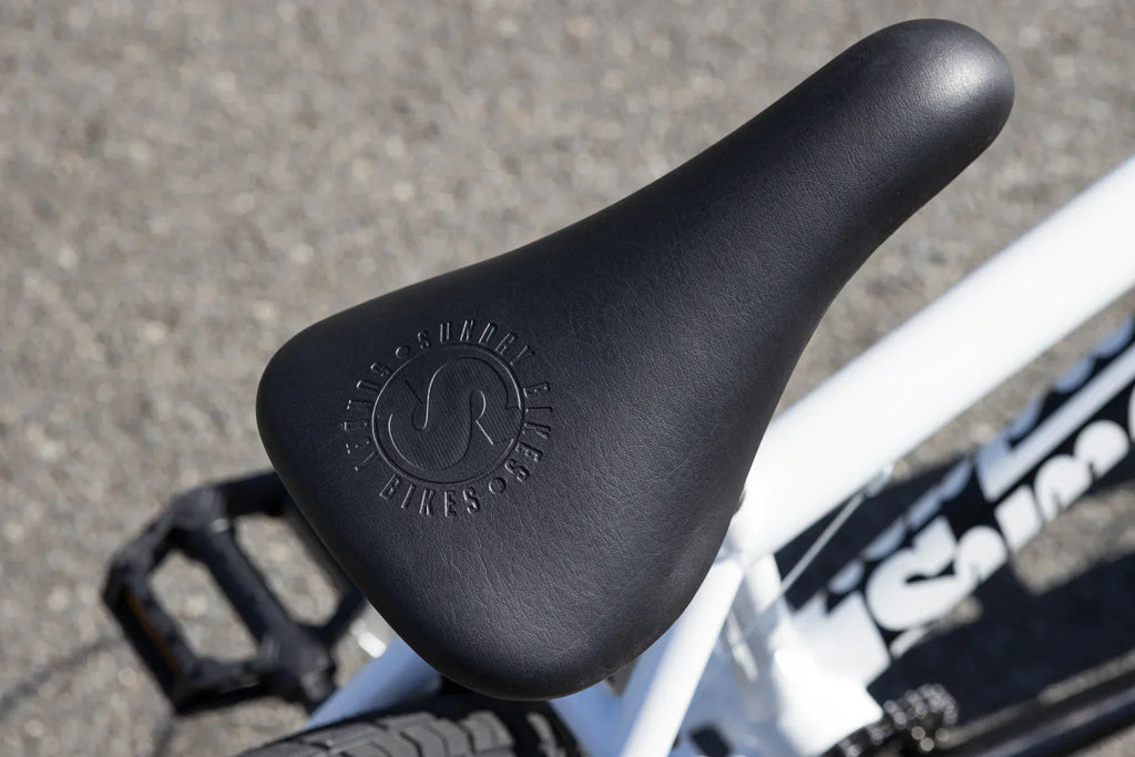 Gros plan d'une selle de vélo BMX noire avec logo embossé sur cadre blanc.