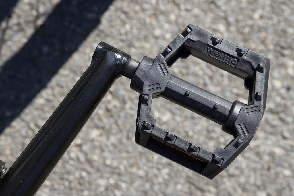 Gros plan d'une pédale de vélo BMX noire en plastique sur un sol en gravier.