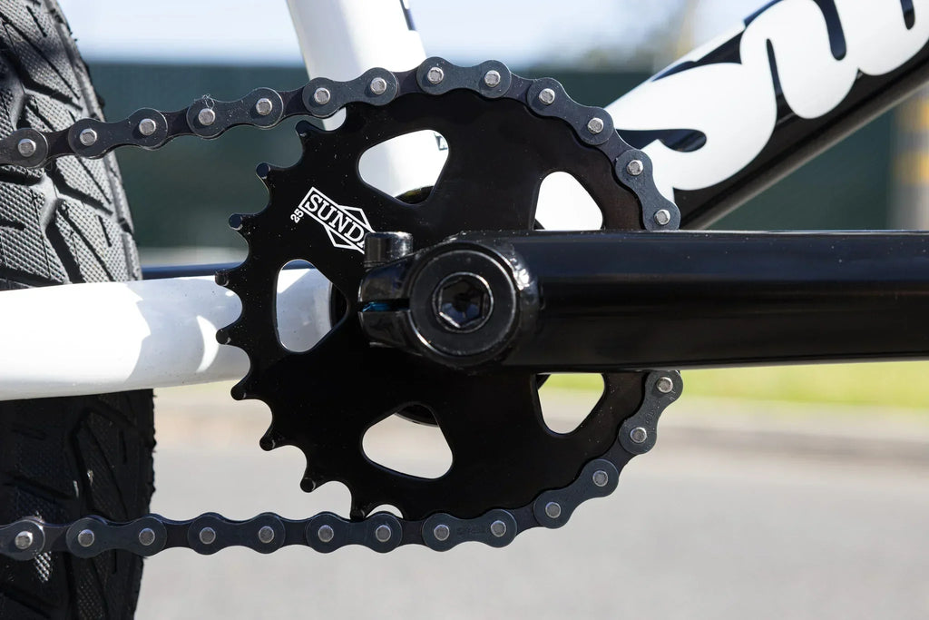 Gros plan d'un plateau Sund noir et d'une chaîne sur un vélo BMX blanc