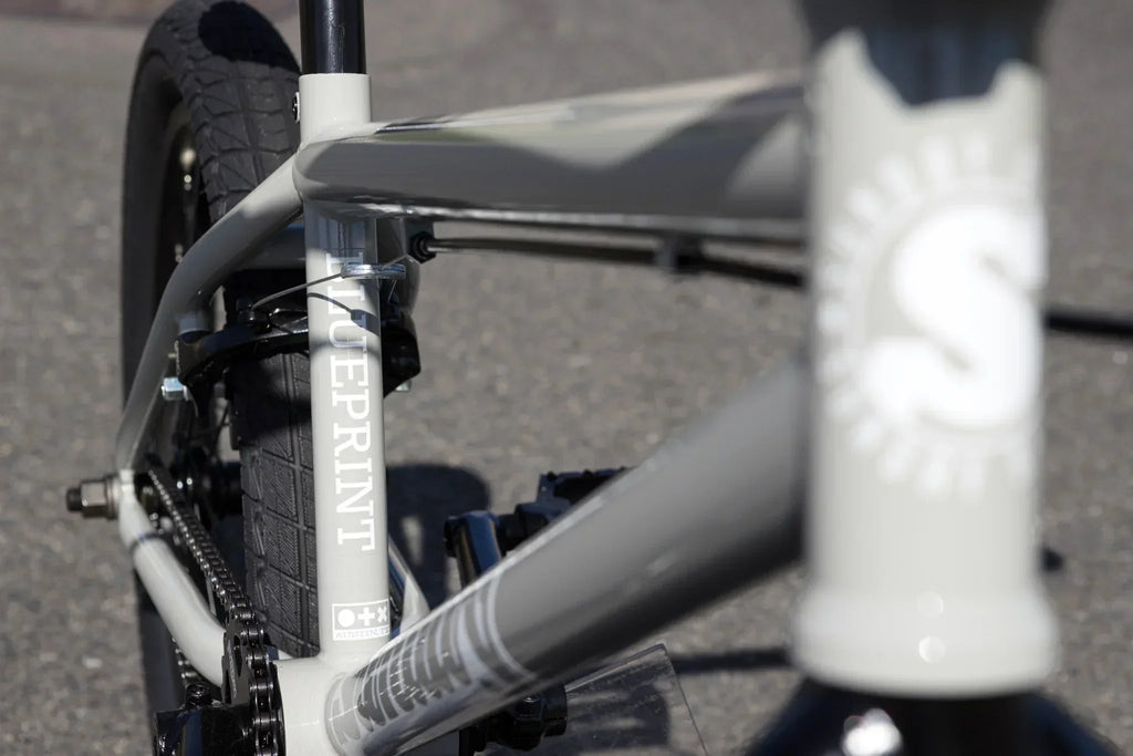 Gros plan du cadre gris d'un vélo BMX Blueprint avec détails du tube et de la chaîne.