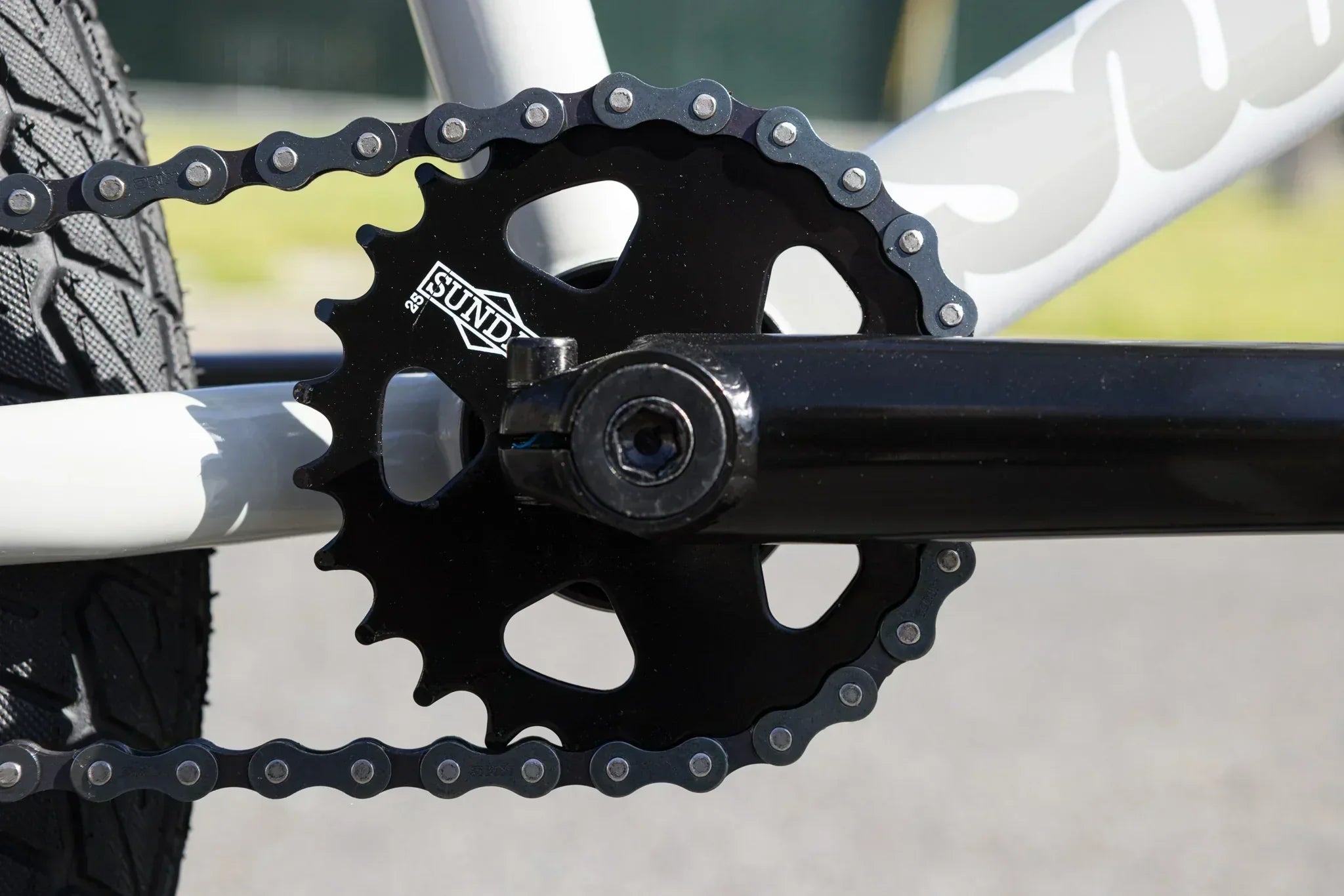 Gros plan d'un plateau Sundae noir et d'une chaîne sur un vélo BMX blanc.