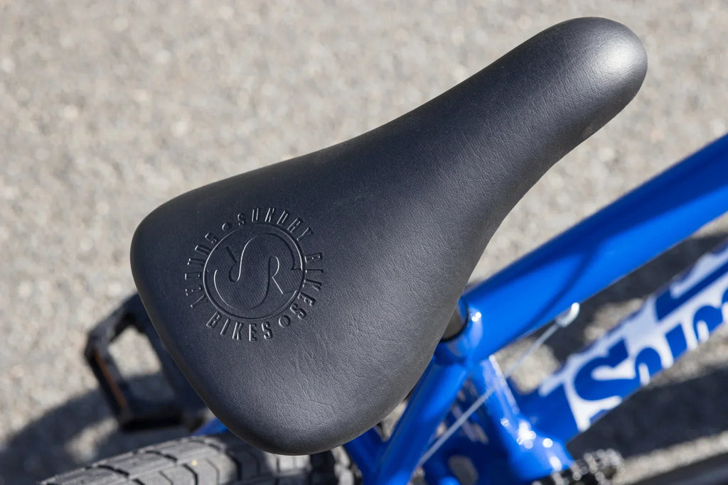 Gros plan d'une selle de vélo BMX noire sur un cadre bleu vif.