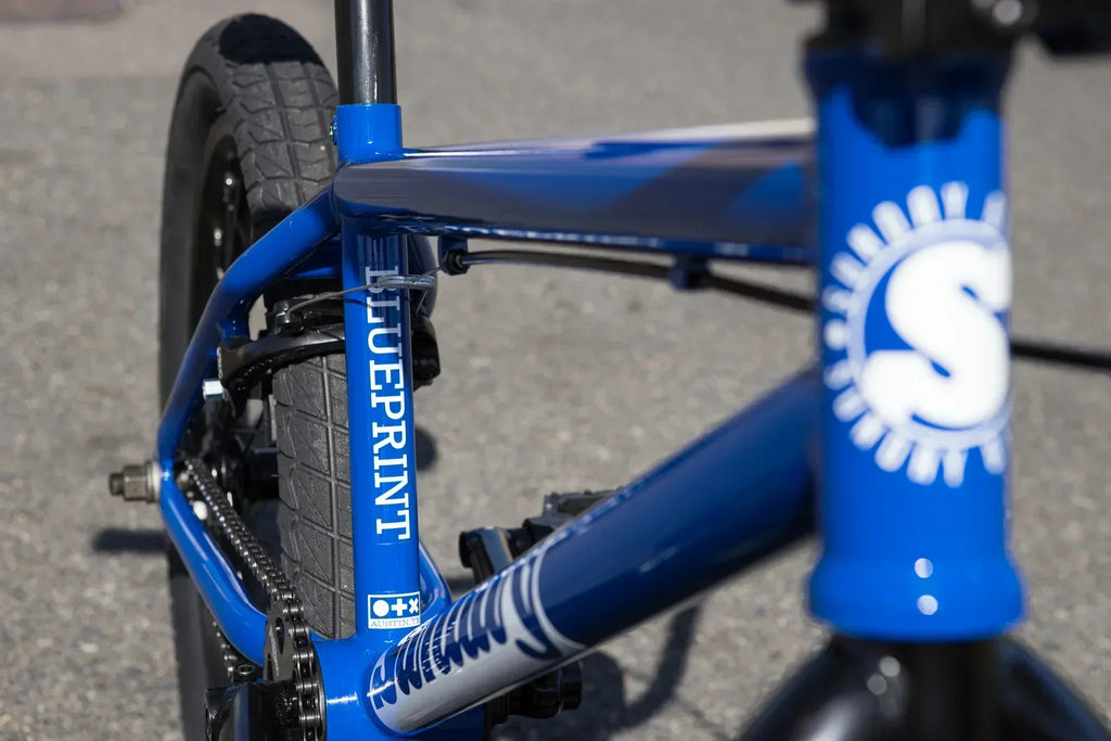 Détail du cadre bleu d'un vélo BMX Blueprint avec pneus noirs