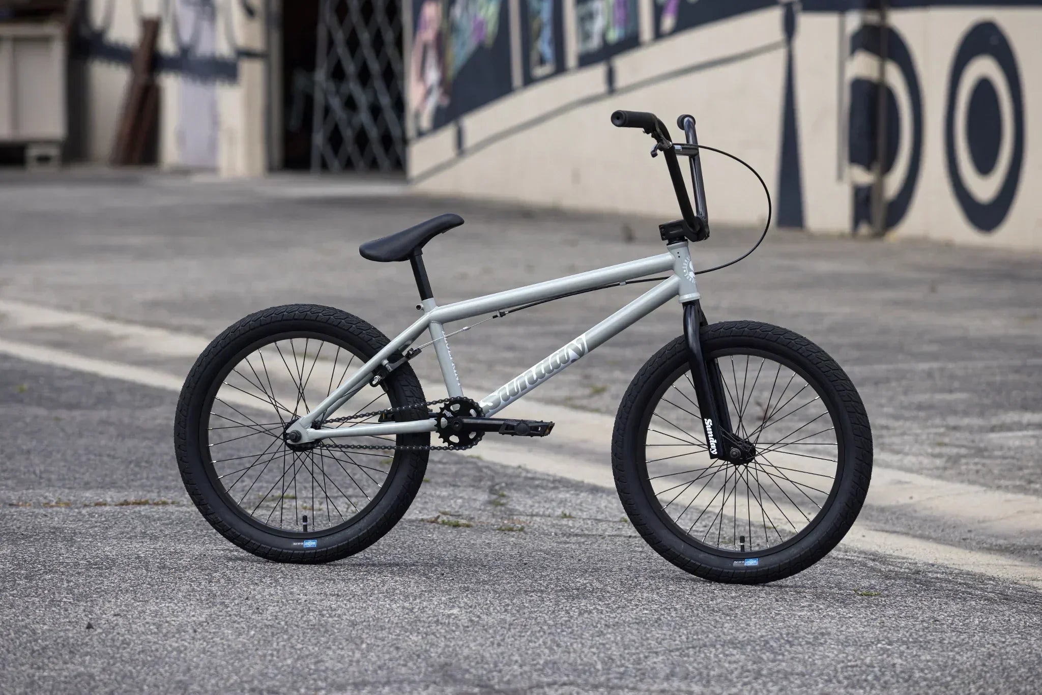 Vélo BMX Sundown gris argenté sur un sol en asphalte