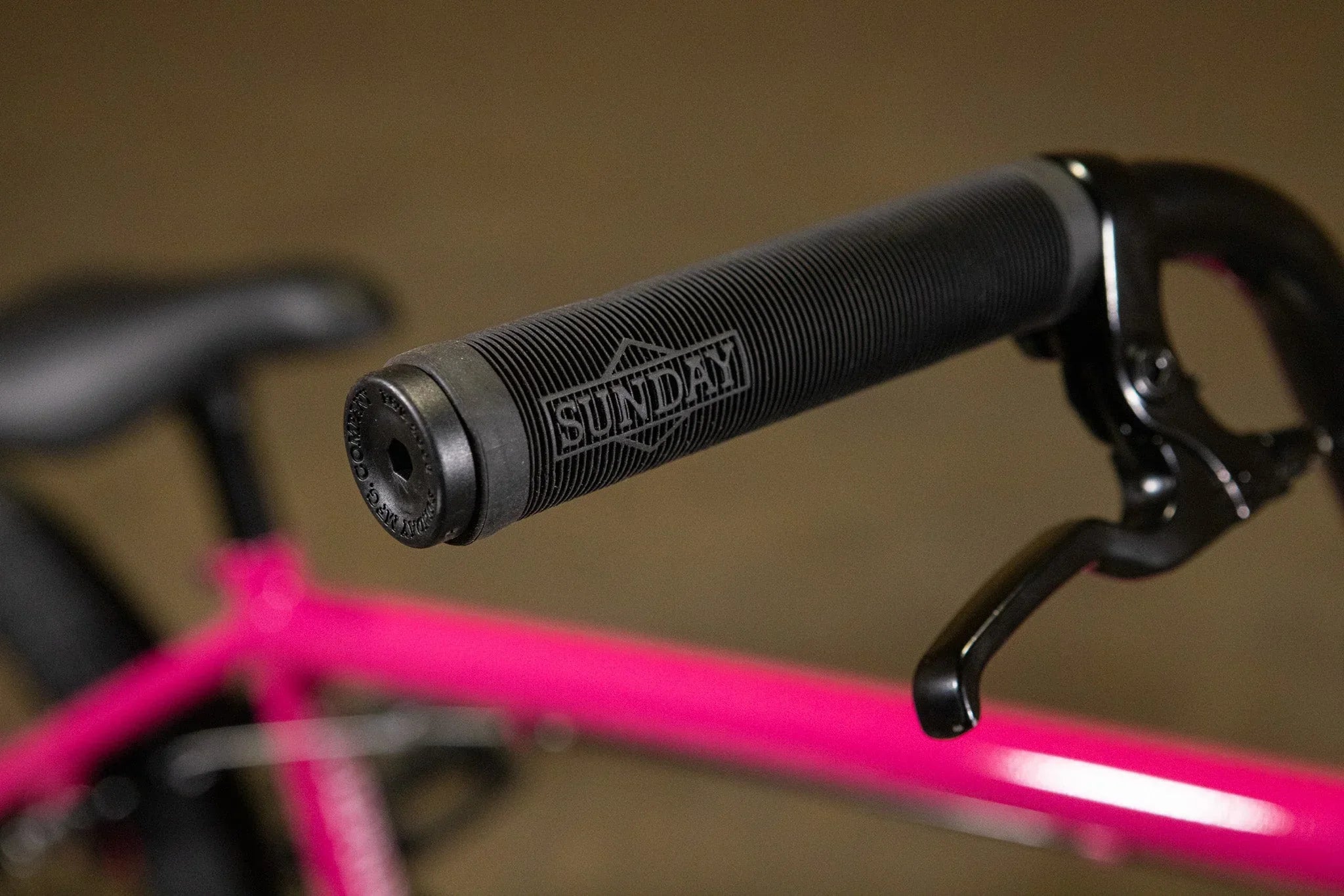 Poignée de guidon BMX noire de marque Sunday sur un cadre de vélo rose vif.