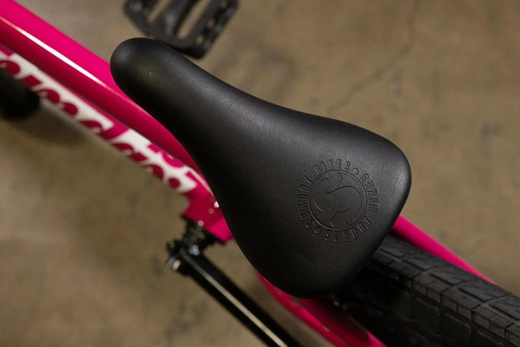 Gros plan d'une selle noire Sundry Bikes sur un cadre de vélo BMX rose vif