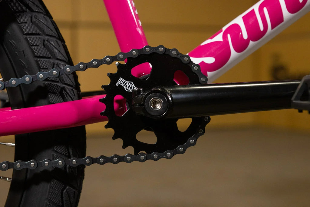 Gros plan du plateau et de la chaîne d'un vélo BMX rose et noir.