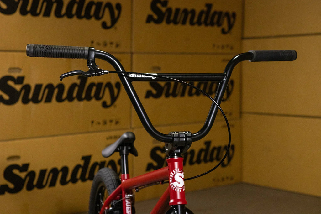 Gros plan du guidon noir d'un vélo BMX rouge devant des cartons Sunday