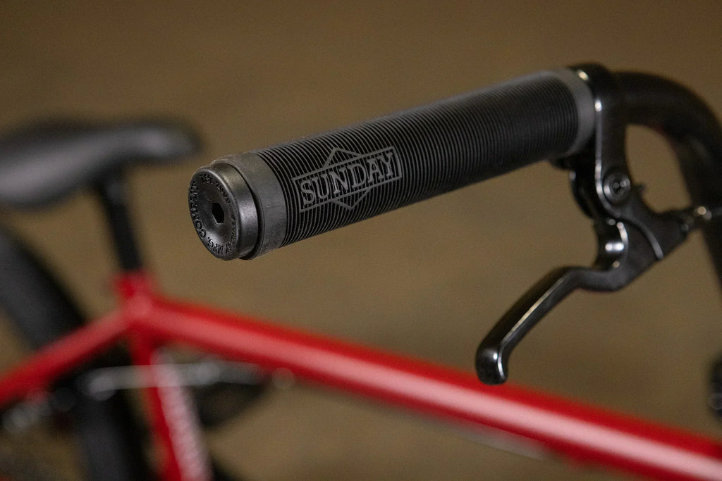 Gros plan d'une poignée de guidon BMX noire avec logo Sunday sur un vélo rouge