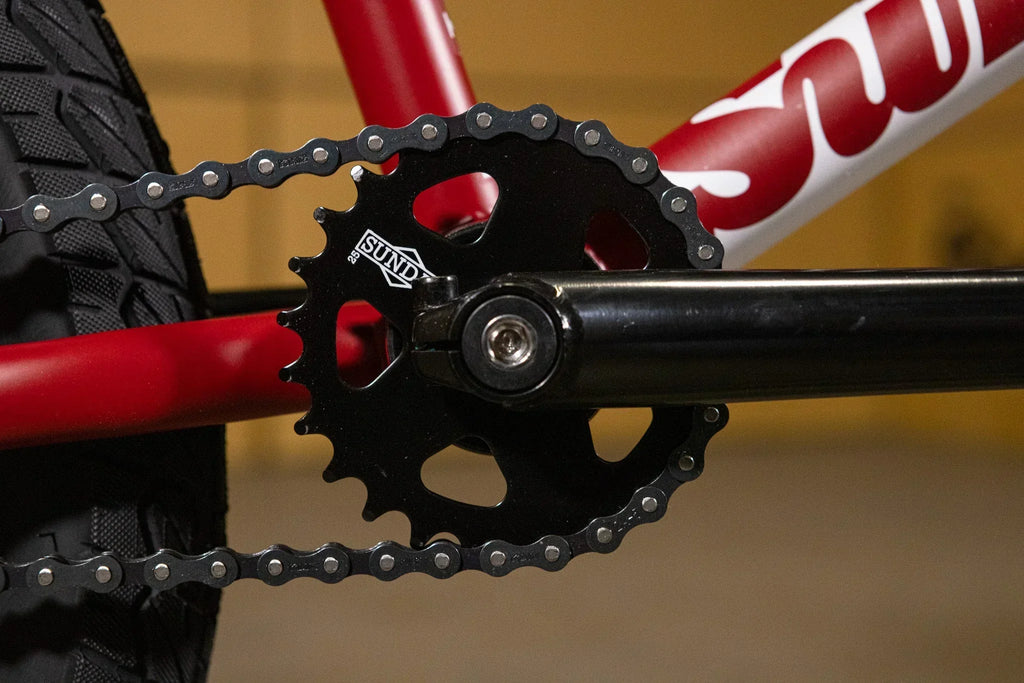 Gros plan d'un plateau Sund noir et d'une chaîne sur un cadre de vélo BMX rouge.