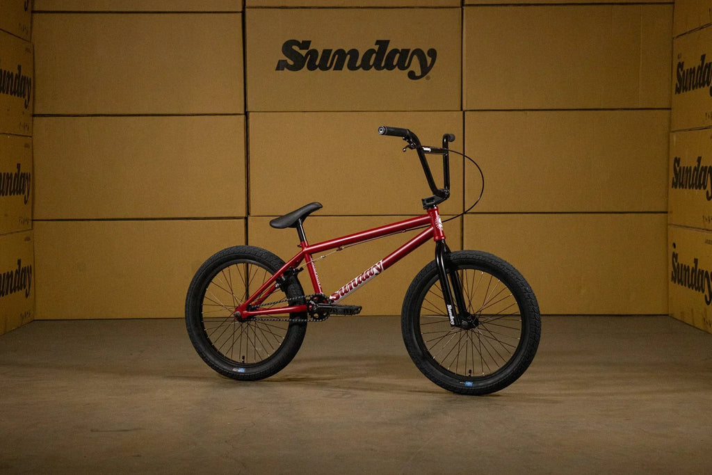 Vélo BMX Sunday rouge avec cadre métallique et pneus noirs sur fond de cartons.
