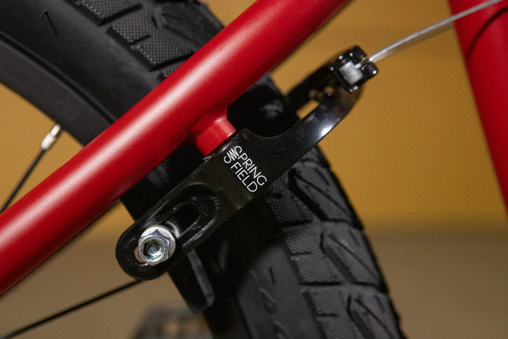 Détail d'un tendeur de chaîne Spring Field noir installé sur un cadre de vélo BMX rouge.
