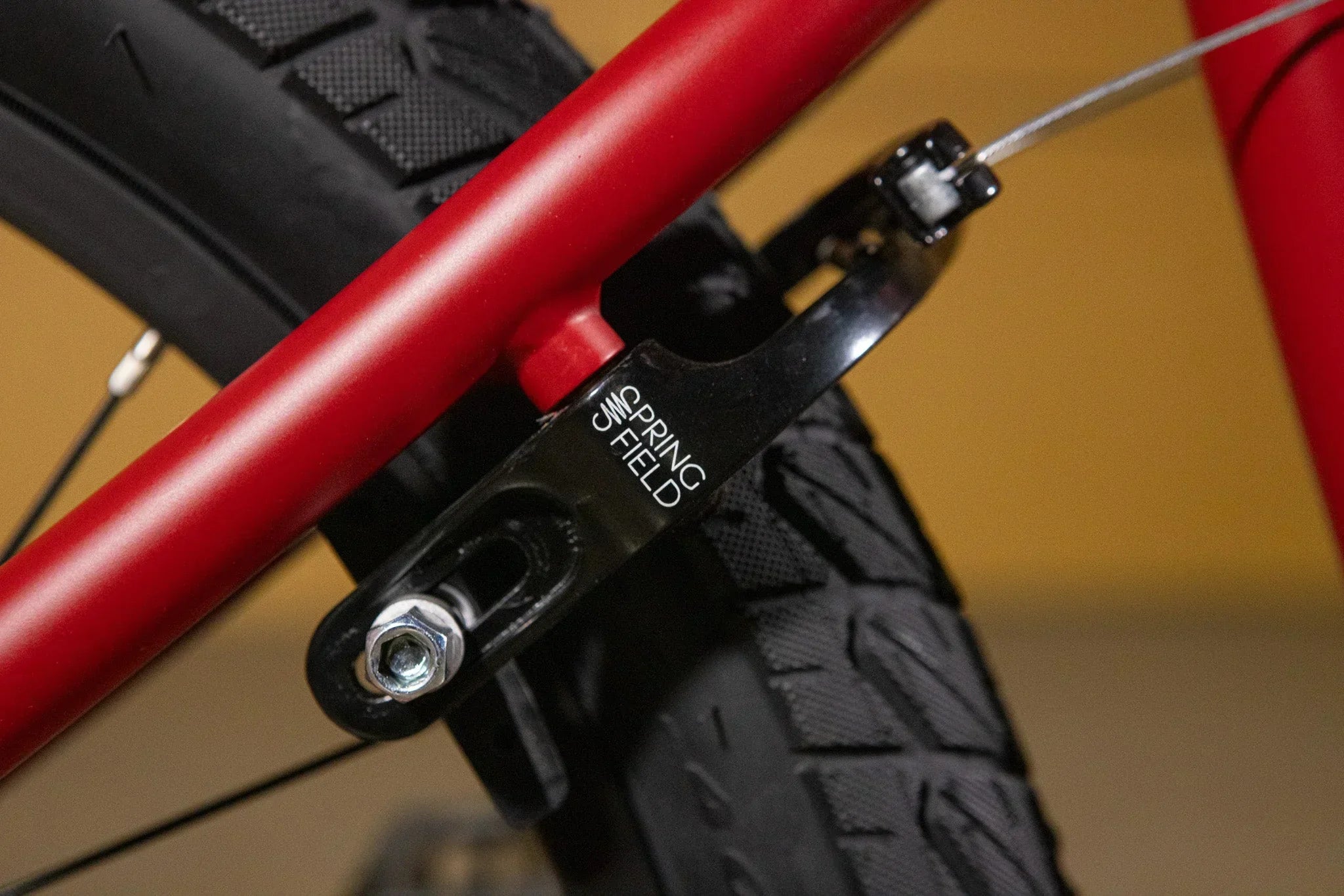 Détail d'un tendeur de chaîne Spring Field noir installé sur un cadre de vélo BMX rouge.