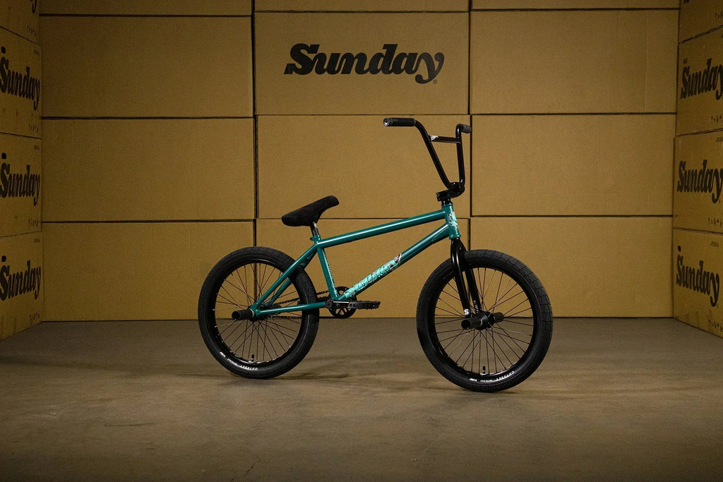 VTT BMX Sunday de couleur turquoise devant des cartons de la marque Sunday