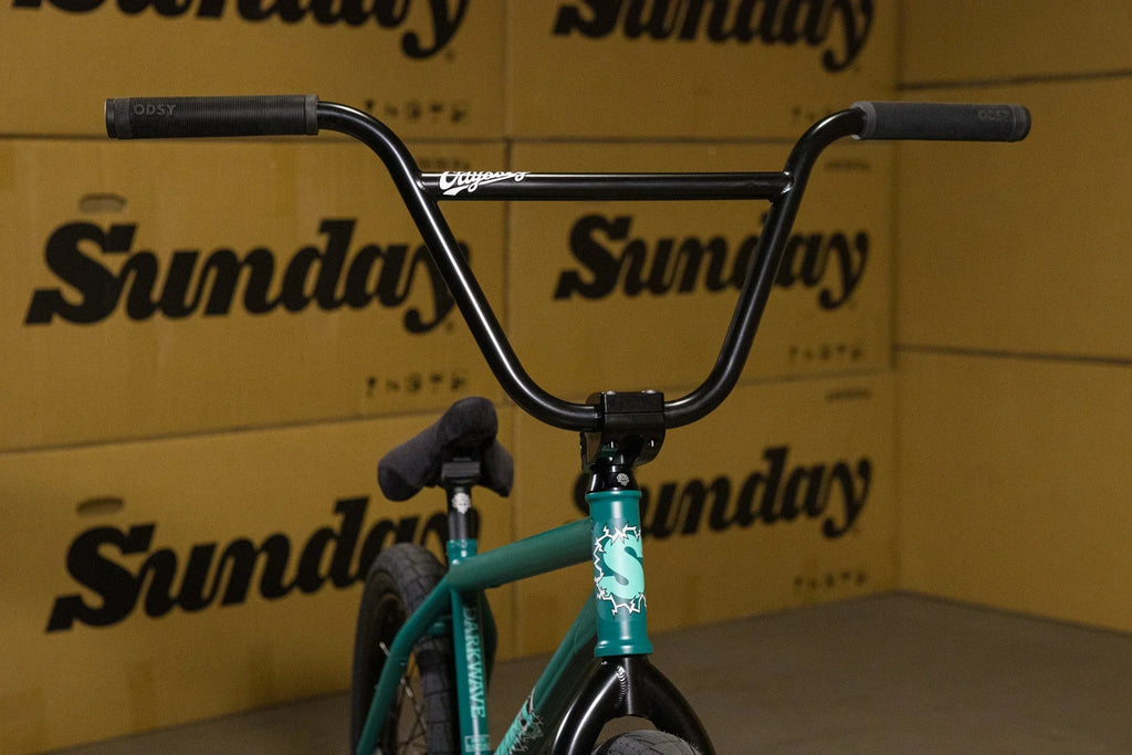 Guidon noir et cadre vert d'un vélo BMX devant des cartons Sunday.