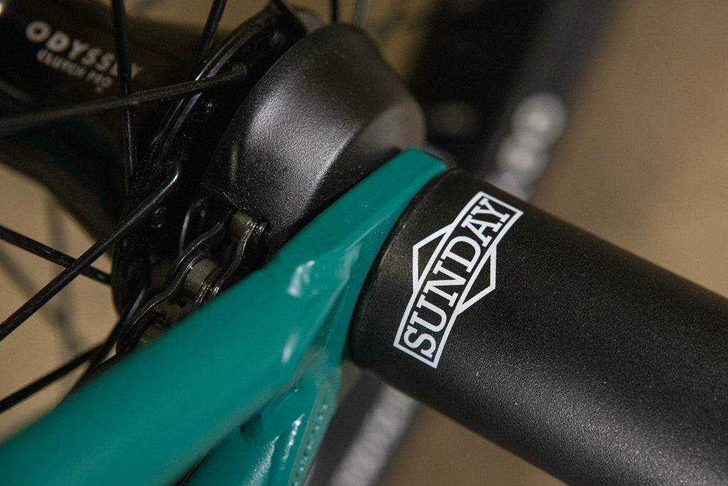 Détail de la tige de selle Sunday noire et du cadre de BMX turquoise.