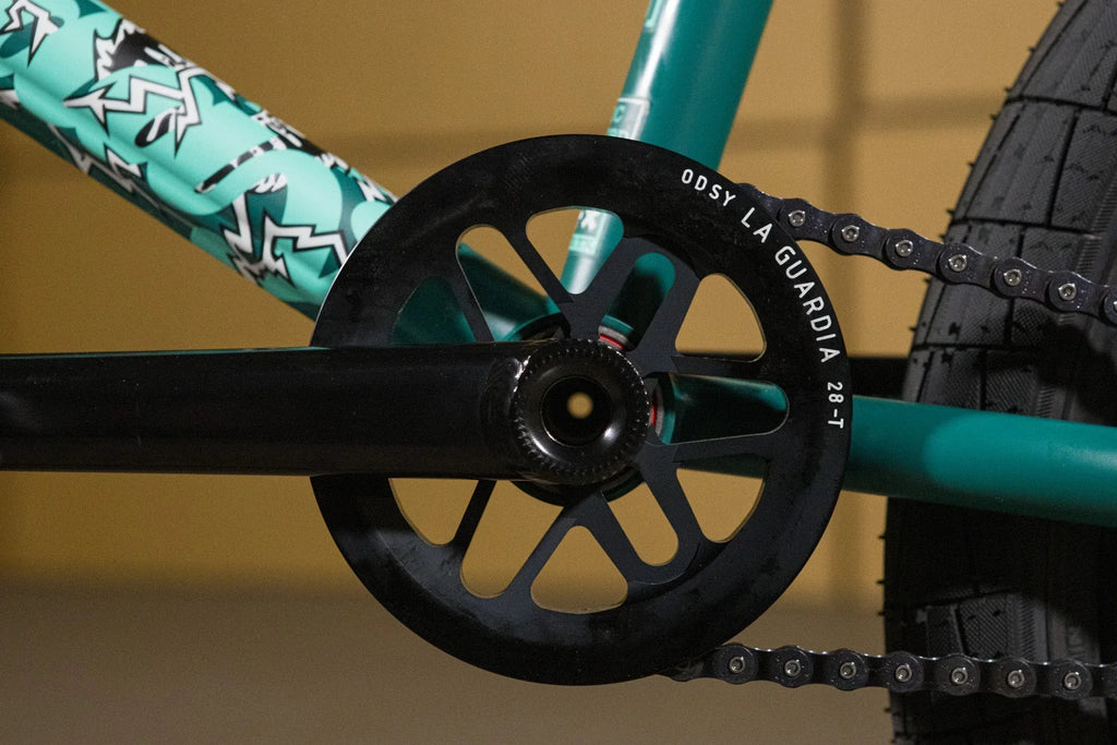 Gros plan d'un plateau Odyssey La Guardia 28T noir sur un vélo BMX turquoise
