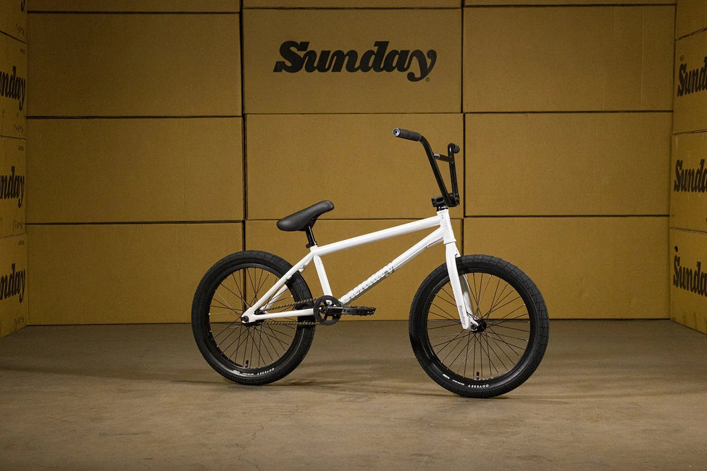 Vélo BMX blanc avec pneus noirs sur fond de cartons Sunday