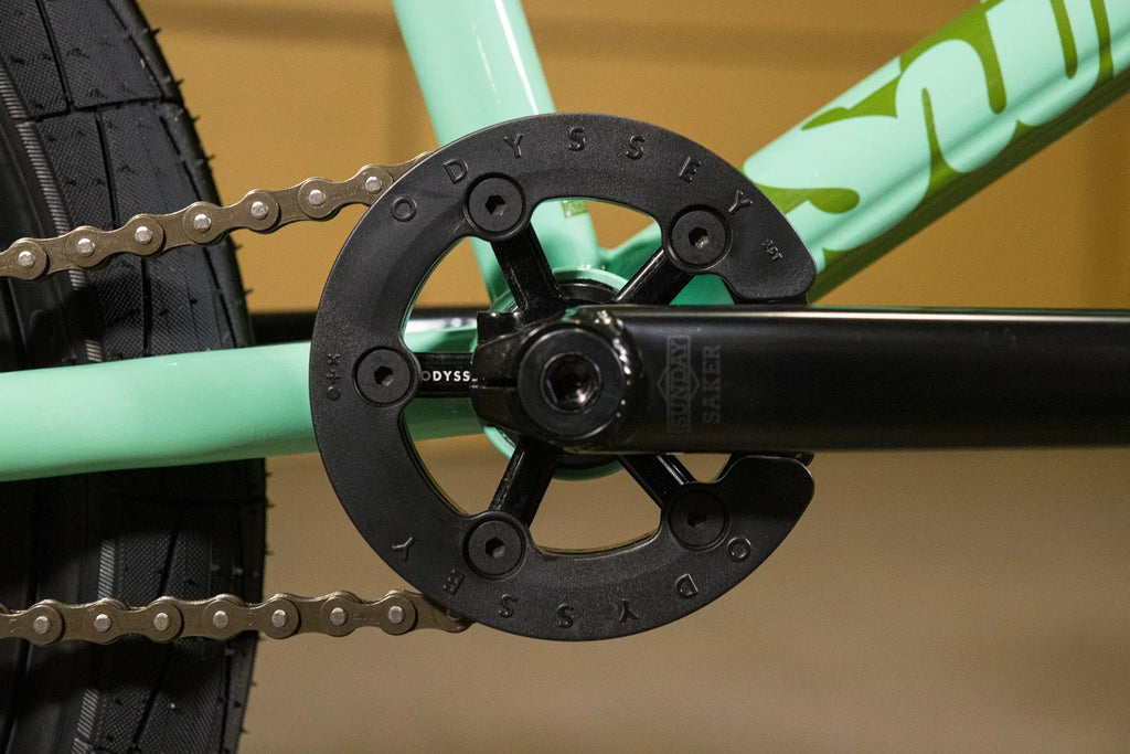 Gros plan d'un plateau Odyssey noir sur un cadre de vélo BMX vert menthe.