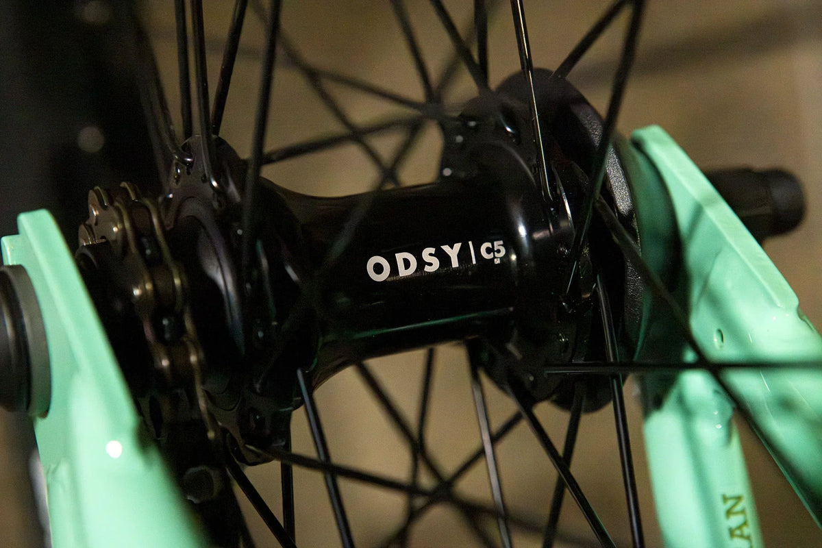 Gros plan d'un moyeu de roue BMX Odys C5 noir sur un cadre vert menthe.