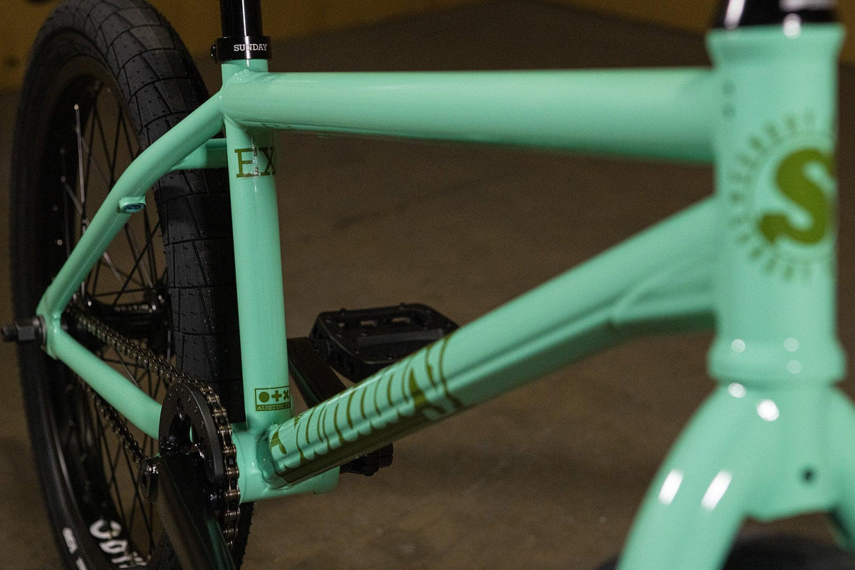 Cadre de vélo BMX vert menthe avec détails graphiques et pédales noires.