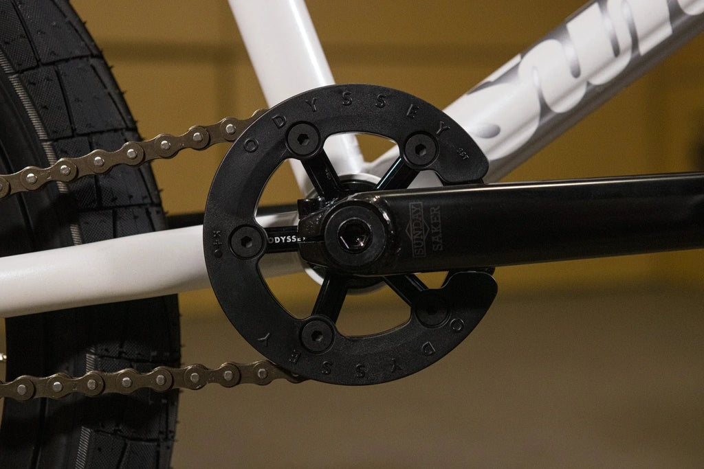 Gros plan d'un plateau Odyssey et pédalier Sunday Saker sur un vélo BMX blanc