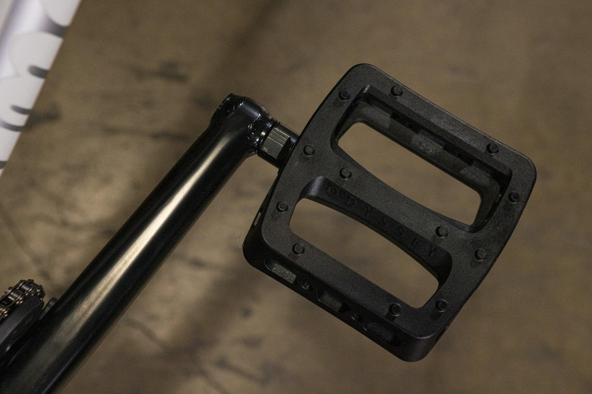 Gros plan d'une pédale de vélo BMX noire de marque Odyssey sur une manivelle.