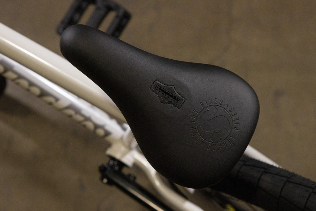 Gros plan d'une selle de vélo BMX noire Sundae Bikes sur un cadre blanc.