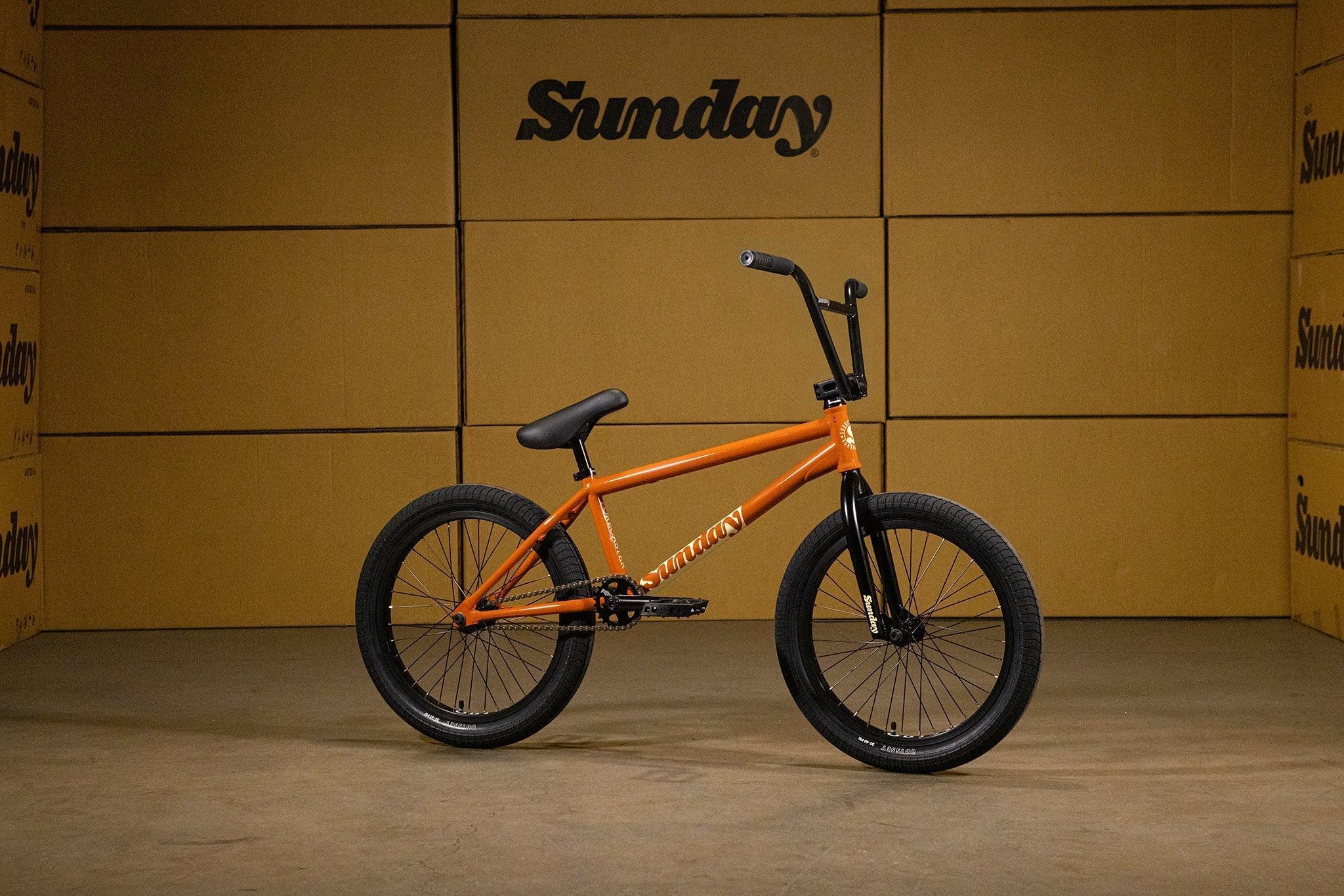 Vélo BMX orange Sunday avec cadre et jantes noires sur fond de cartons