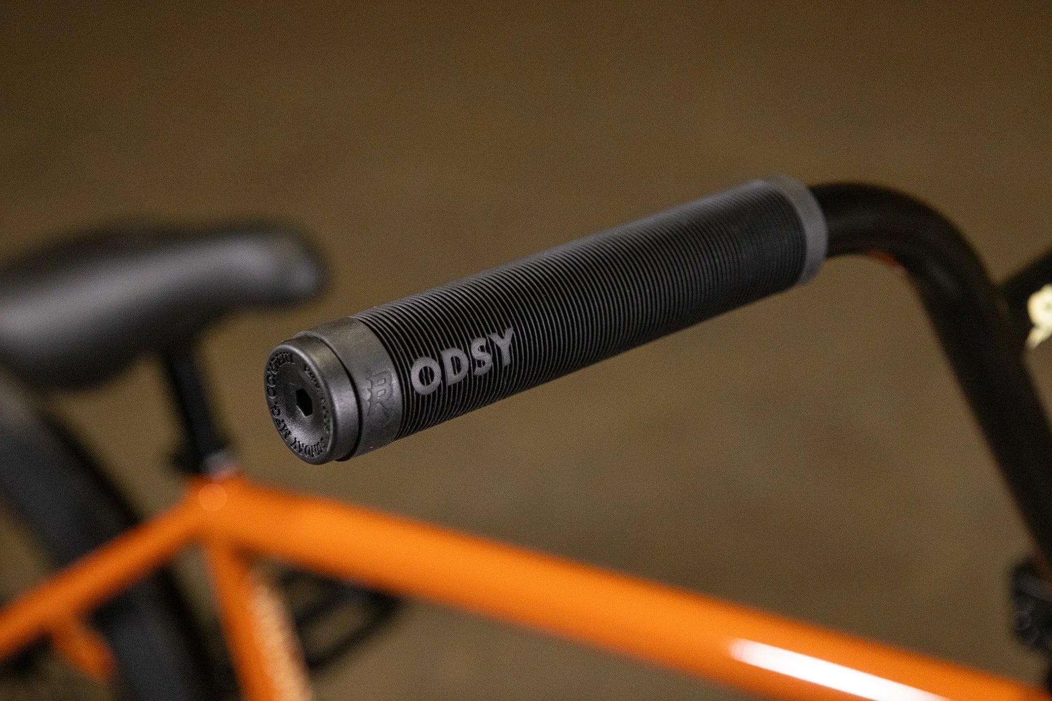 Gros plan d'une poignée de guidon BMX noire texturée de marque Odys sur un cadre orange.