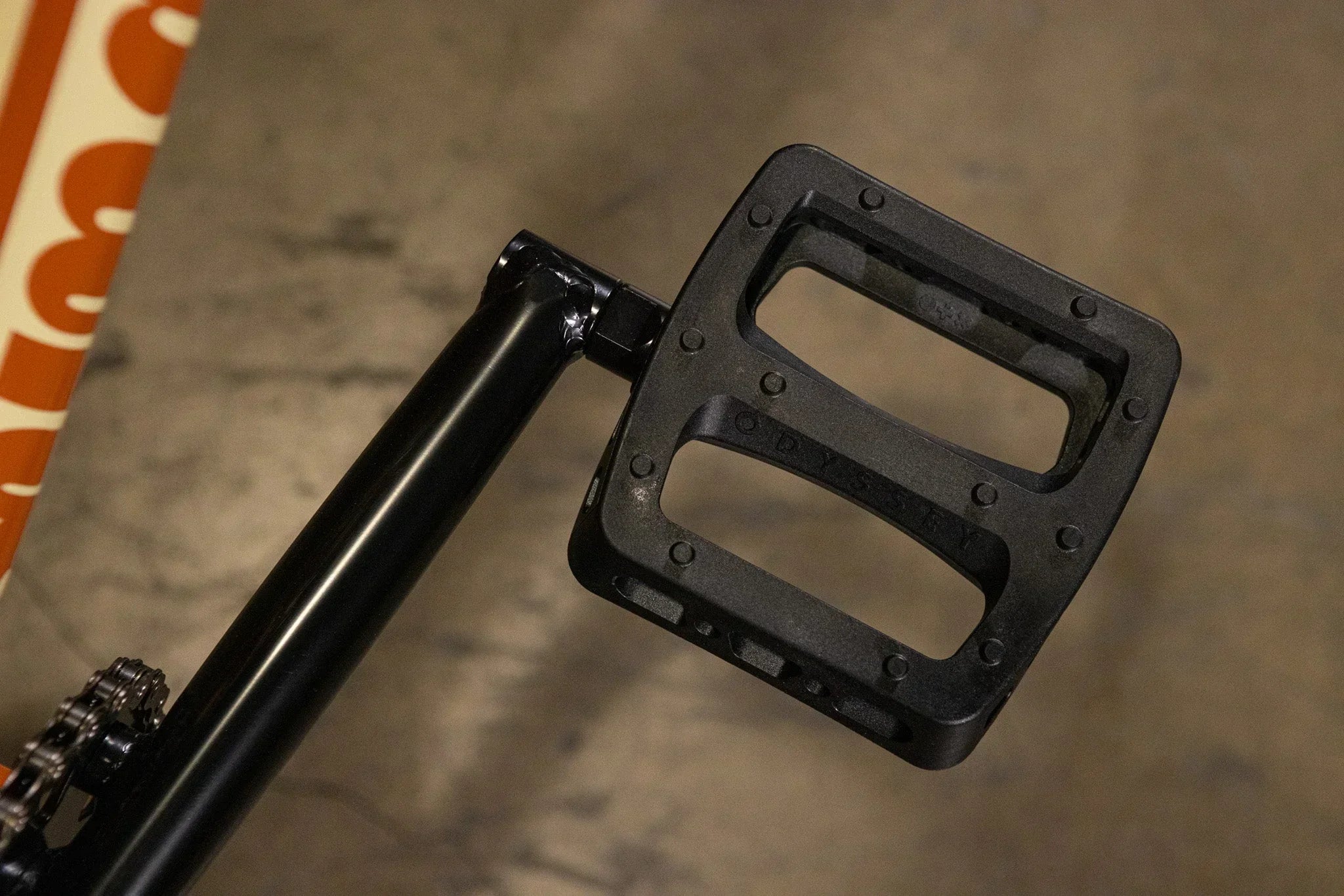 Gros plan d'une pédale de BMX noire Odyssey sur un cadre de vélo noir.