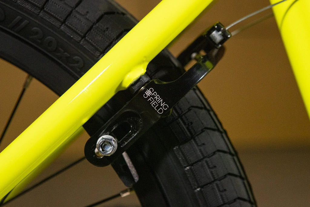 Gros plan d'un frein Spring Field noir sur un cadre de BMX jaune fluo