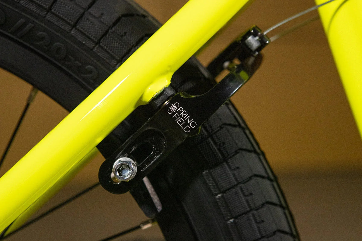 Gros plan d'un frein Spring Field noir sur un cadre de BMX jaune fluo