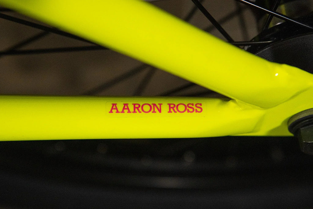 Détail d'un cadre de vélo BMX jaune fluo avec l'inscription AARON ROSS en rouge.
