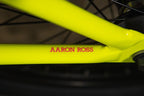 Détail d'un cadre de vélo BMX jaune fluo avec l'inscription AARON ROSS en rouge.