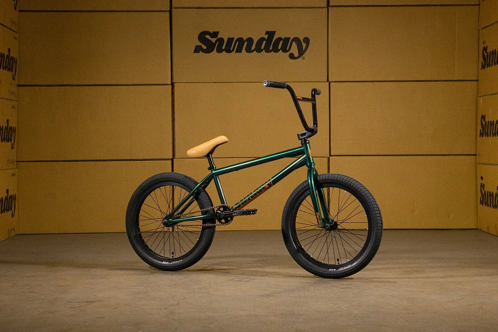 Vélo BMX vert avec selle beige et guidon noir sur fond de cartons Sunday