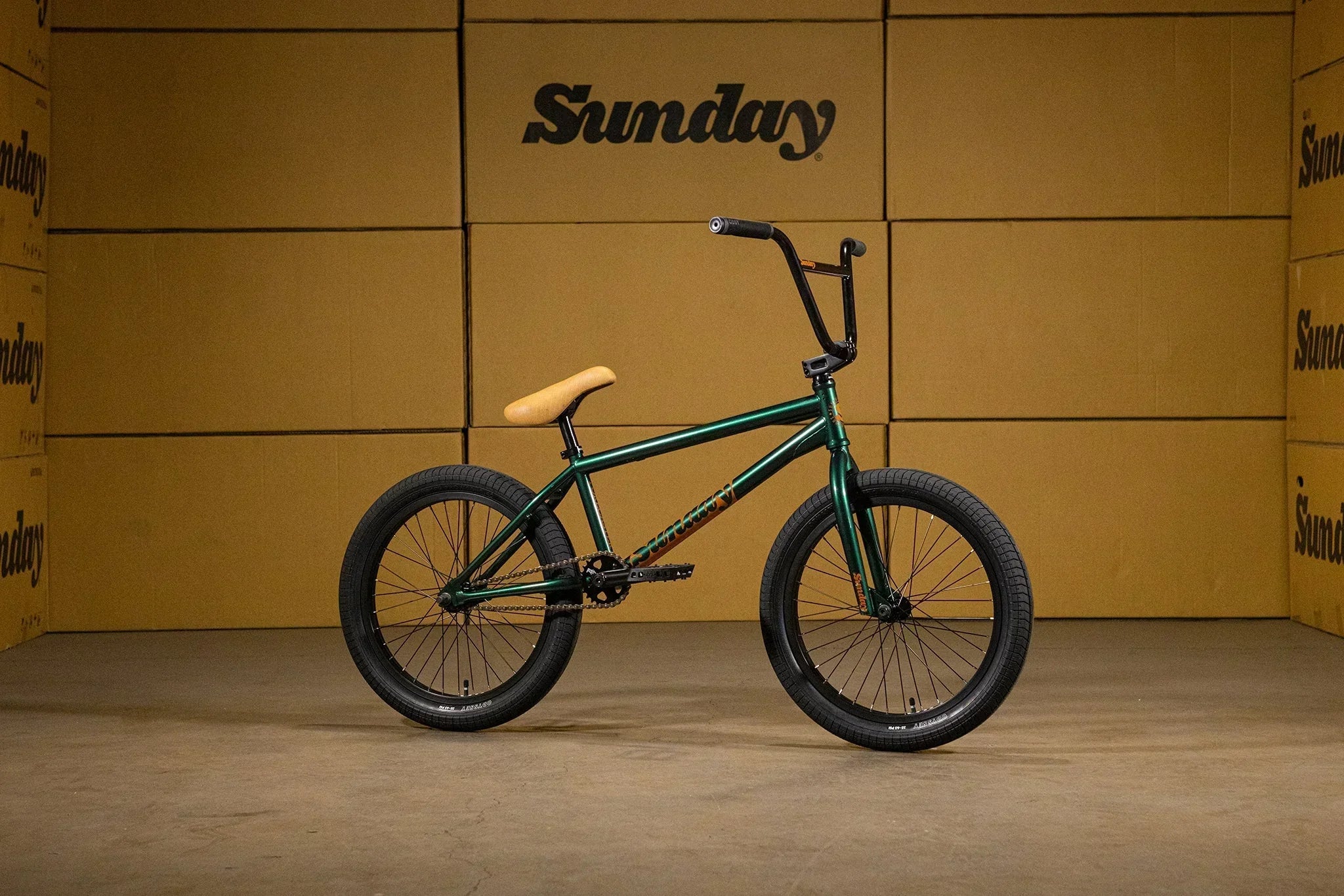 Vélo BMX vert avec selle beige et guidon noir sur fond de cartons Sunday
